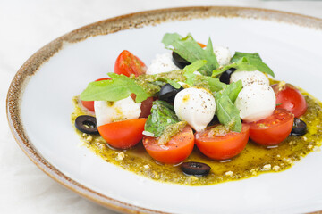 Wall Mural - Caprese salad with fresh cherry tomatoes, mini mozzarella, pesto, basil, olive oil and balsamic sauce on a white plate and on a white background Mediterranean diet concept. Italian healthy food.