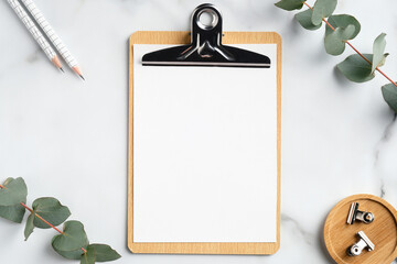 Mockup of wooden clipboard with blank paper on marble table with office supplies and eucalyptus branches. Top view with copy space, flat lay.
