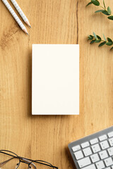 Fototapete - White empty paper card on wooden office desk table with keyboard, glasses, pencils, eucalyptus. Flat lay, top view, copy space.