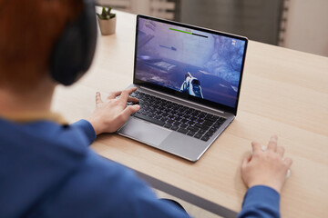 Wall Mural - High angle portrait of unrecognizable teenage boy playing video games via laptop and wearing headphones, copy space