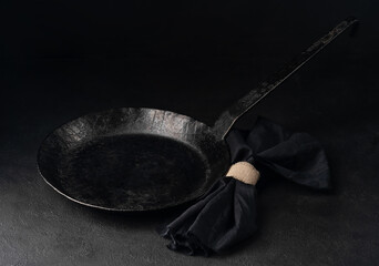 Vintage forged empty carbon steel frying pan, with napkin on black background.