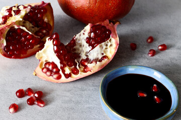 Pomegranate molasses in small bowl. Pomegranate sweet and sour syrup with pomegranate fruit and seeds on gray background.