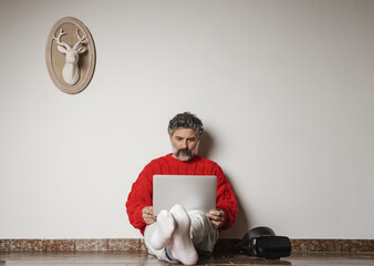 Poster - Adult male with a red sweater sitting on the floor and working on his laptop