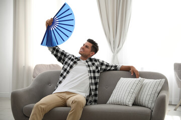 Poster - Man with hand fan sitting on sofa. Summer season