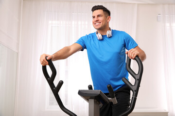 Poster - Man with headphones using modern elliptical machine at home