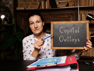 Wall Mural - Young woman holding a black chalkboard in hands. Conceptual photo about Capital Outlays with written text.