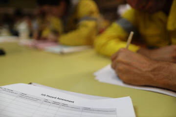 Wall Mural - clear image of job risk assessment booklet placing on the table with defocused construction worker h