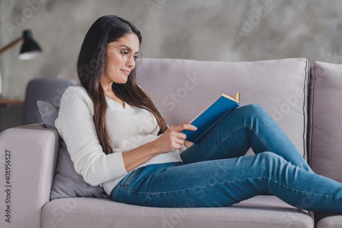 Photo of calm girl lay sofa relax read textbook wear spectacles white sweater in living room home indoors