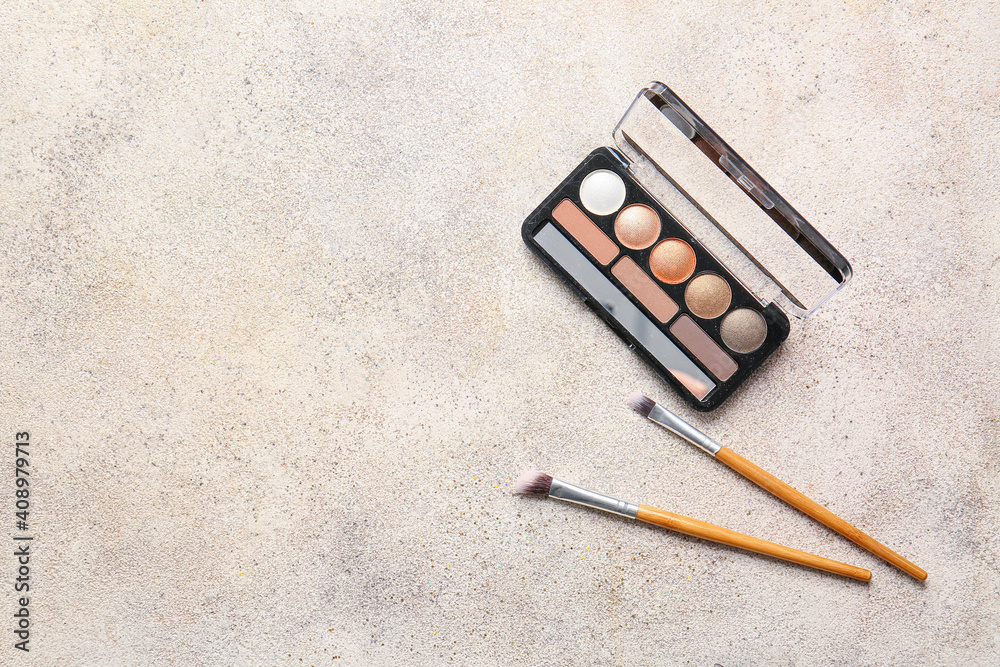 Beautiful palette of eyeshadows and brushes on light background