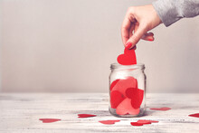 A Woman Puts Another Red Heart In A Glass Jar With Hearts. Valentine's Day Greeting Card. Collection Of Likes