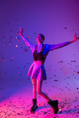 Poster - full length of happy woman in stylish outfit with outstretched hands near falling confetti on purple