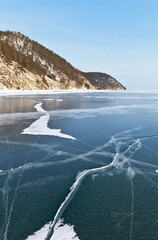 Beautiful winter landscape with blue ice with cracks and coastal mountains. Frozen Lake Baikal in January on a sunny cold day. Natural background. Winter holidays and ice travel