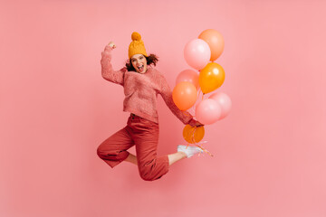 Wall Mural - Positive girl in hat jumping and laughing. Blissful young woman dancing with party balloons.