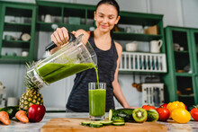 Slim Young Girl Cooking Green Fresh Smoothie In Blender In The Kitchen