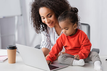 Wall Mural - toddler african american child typing on laptop near cheerful mother
