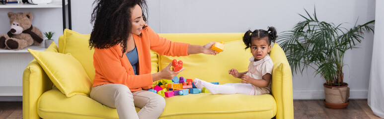 Wall Mural - happy african american mother playing building blocks with toddler kid on sofa, banner