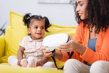 Wall Mural - happy african american mother holding vr headset near daughter in living room