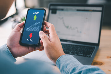 Wall Mural - Hand of trader holding smartphone looking at Stock exchange trading data information displayed with buy and sell symbol. Investor and trader concept.