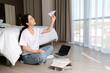 © _KUBE_ - The concept of online courses and online messengers. A young woman sits cross-legged on the floor and launches a paper airplane into the air. On the floor is a laptop and books