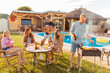 © Impact Photography - Friends grilling meat, playing the guitar and singing at poolside backyard barbecue party