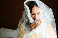 Laughing teen girl with braces wrapped in bubble wrap hiding and popping bubbles
