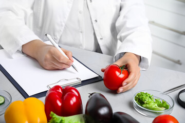 Wall Mural - scientist with clipboard and fresh tomato at table in laboratory, closeup. poison detection