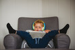 © Cavan Images - Child inside during isolation playing with tablet feet up on couch