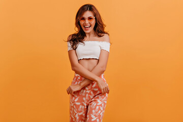 Canvas Print - Emotional positive lady in orange pants crossed her arms and poses for portrait, laughing and having fun in studio