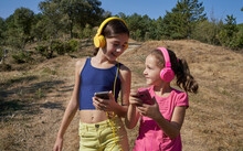 Little Girls Listening To Music And Singing With Yellow And Pink Headphones In A Garden. Music Concept