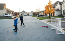 Two Boys Playing Street Hockey On A Residential Street In The Fall.