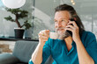© Cavan Images - Mature man with beard talking on the phone and drinking coffee sitting