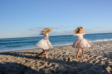 Two Girls Spinning On The Beach With Blue Skies Behind Them