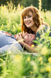 young beautiful couple red-haired girl in a pink dress and green jacket a man in a gray t-shirt and green shorts are having fun in the grass in a field in nature at sunset