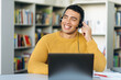 © Kateryna - Successful male employee at online briefing. Satisfied smiling hispanic call center operator, wearing headphones, communicates with clients, looks away and friendly smiles
