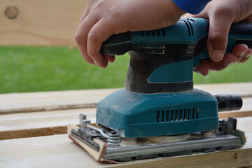 Carpenters Grinds Board With Orbital Sander