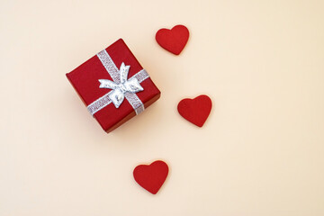 On a yellow background there is a red gift box next to three red hearts.A greeting card. Holiday background