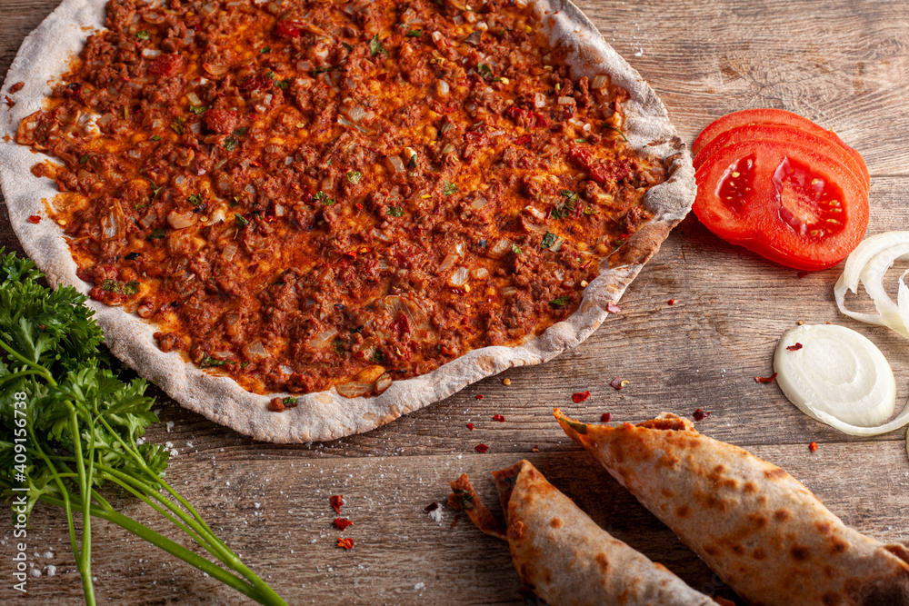 Traditional Turkish Pizza known as Lahmacun made with thin flat dough covered with mixture containing ground beef and baked in stone oven. It is served with parsley, tomatoes and onions on wood. - obrazy, fototapety, plakaty 