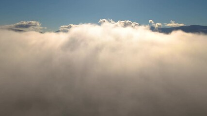 Wall Mural - Aerial reveal shot of yellow sunset over white puffy clouds with distant mountains on horizon.