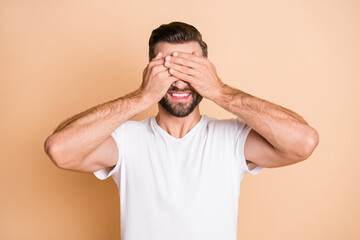 Wall Mural - Photo of young handsome man happy positive smile close cover eyes hands childish playful isolated over beige color background