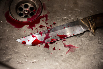 A bloody knife lying in the sink, stained with drops of blood.