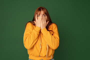 Wall Mural - Scared. Caucasian woman's portrait isolated on green studio background with copyspace. Beautiful female model in yellow sweatshirt. Concept of human emotions, facial expression, sales, ad, fashion.