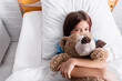 © LIGHTFIELD STUDIOS - top view of child hugging teddy bear while lying in bed and looking at camera