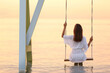 © New Africa - Young woman enjoying sunrise on swing over water