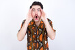 © Roquillo - Young caucasian man wearing generic pattern printed shirt against white wall with scared expression, keeps hands on head, jaw dropped, has terrific expression. Omg concept