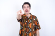 © Roquillo - Young caucasian man wearing generic pattern printed shirt against yellow wall Pointing with finger surprised ahead, open mouth amazed expression, something on the front.