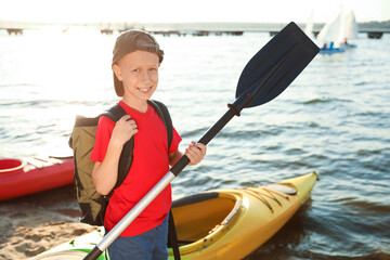 Poster - Happy boy with paddle near kayak on river shore. Summer camp activity