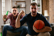 © JustLife - Two young friends enjoying at home. Men drinking beer and watching sports game on tv.