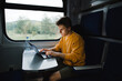 A freelancer man sitting in a train at a table and working on a laptop with a serious face. Freelancer uses laptop on the way by train. Working in travel.