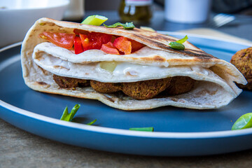 Fresh gluten free tortilla wrap stuffed with chickpea falafel, fresh vegetables chopped salad, fried onion rings, jalapenos, mayo and scallions. Healthy and tasty meal preparation. Side view.