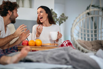 Wall Mural - A young couple loves chatting while having a breakfast in the bed. Love, relationship, together